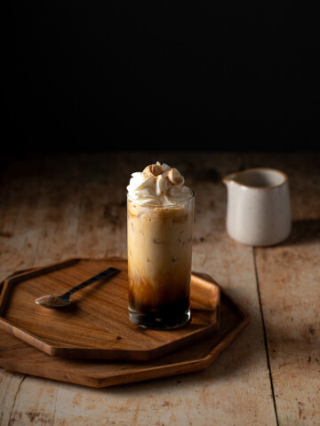 iced cinnamon dolce latte topped with whipped cream on a wooden tray