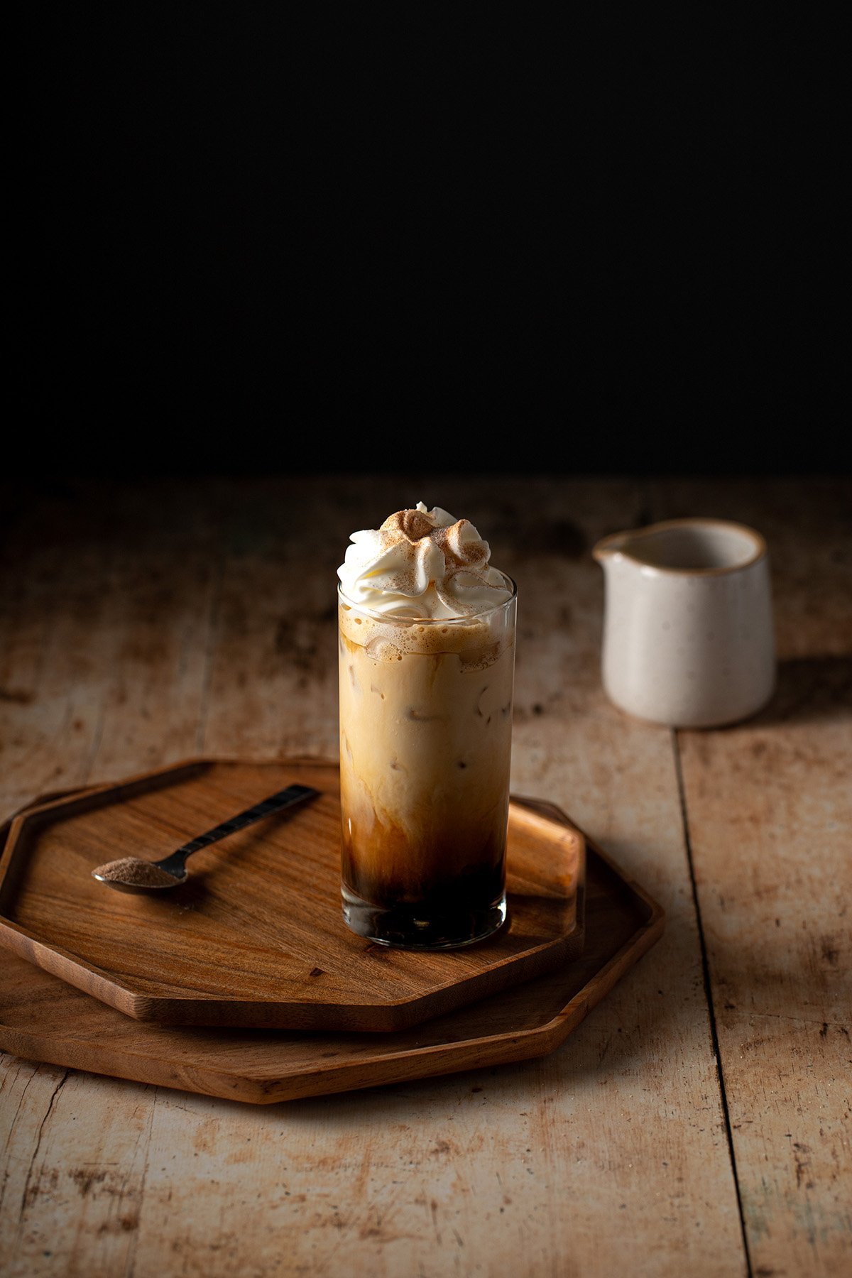 Ice coffee in glass mug with milk and cinnamon on wooden table in