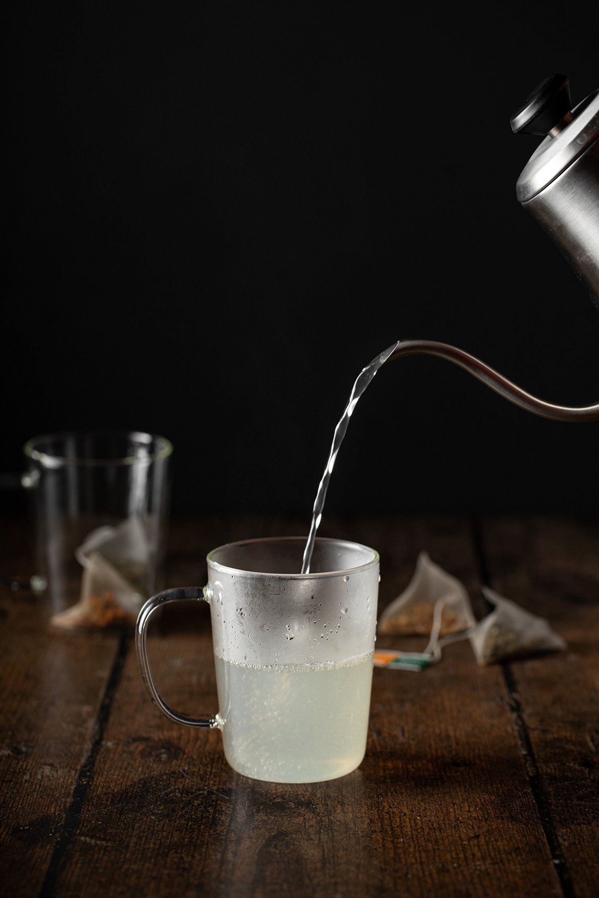 water and lemonade being poured out of a gooseneck kettle into a glass mug