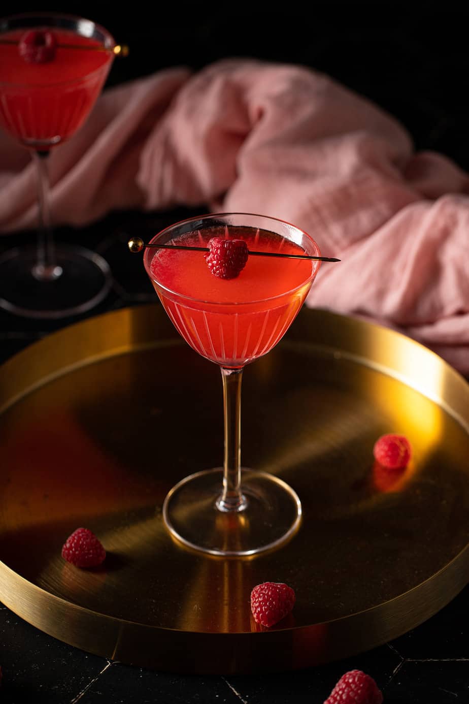 close up of a nick and nora glass with raspberry martini in it on a gold tray