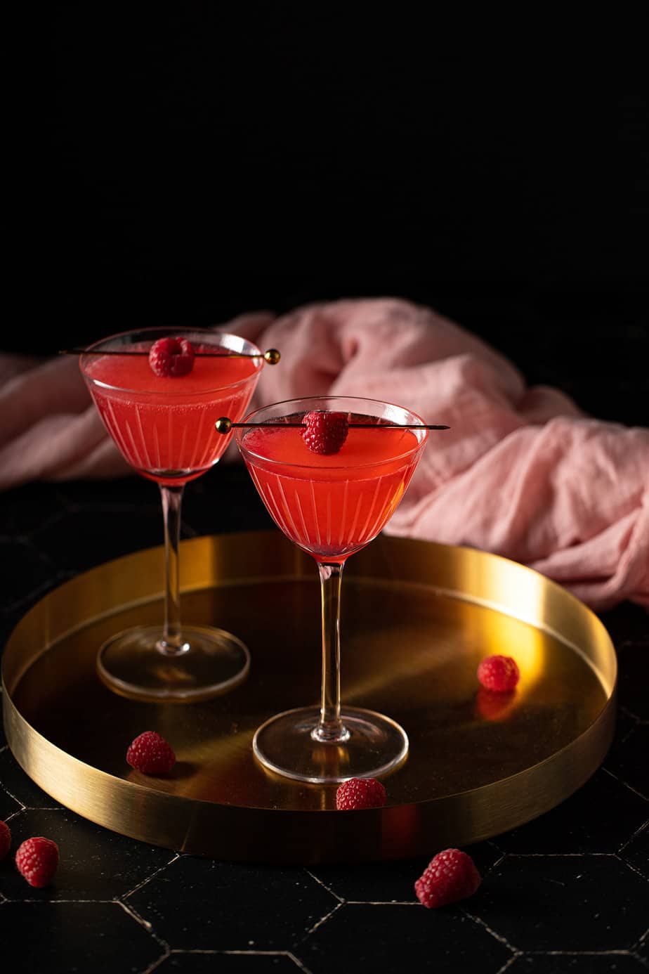 two nick and nora glasses with raspberry martinis on a gold tray