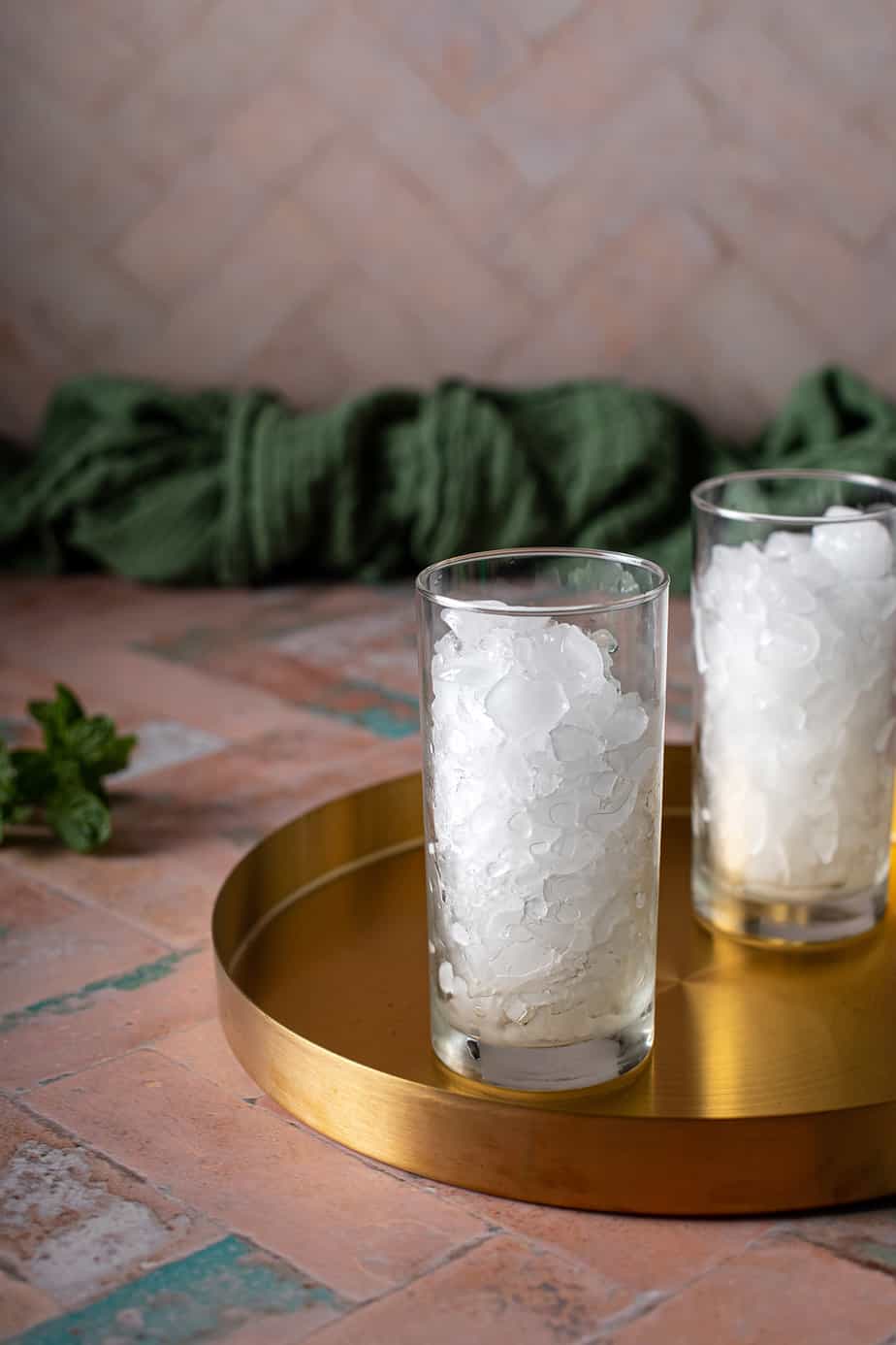two tall glasses filled with crushed ice, sitting on a gold drink tray