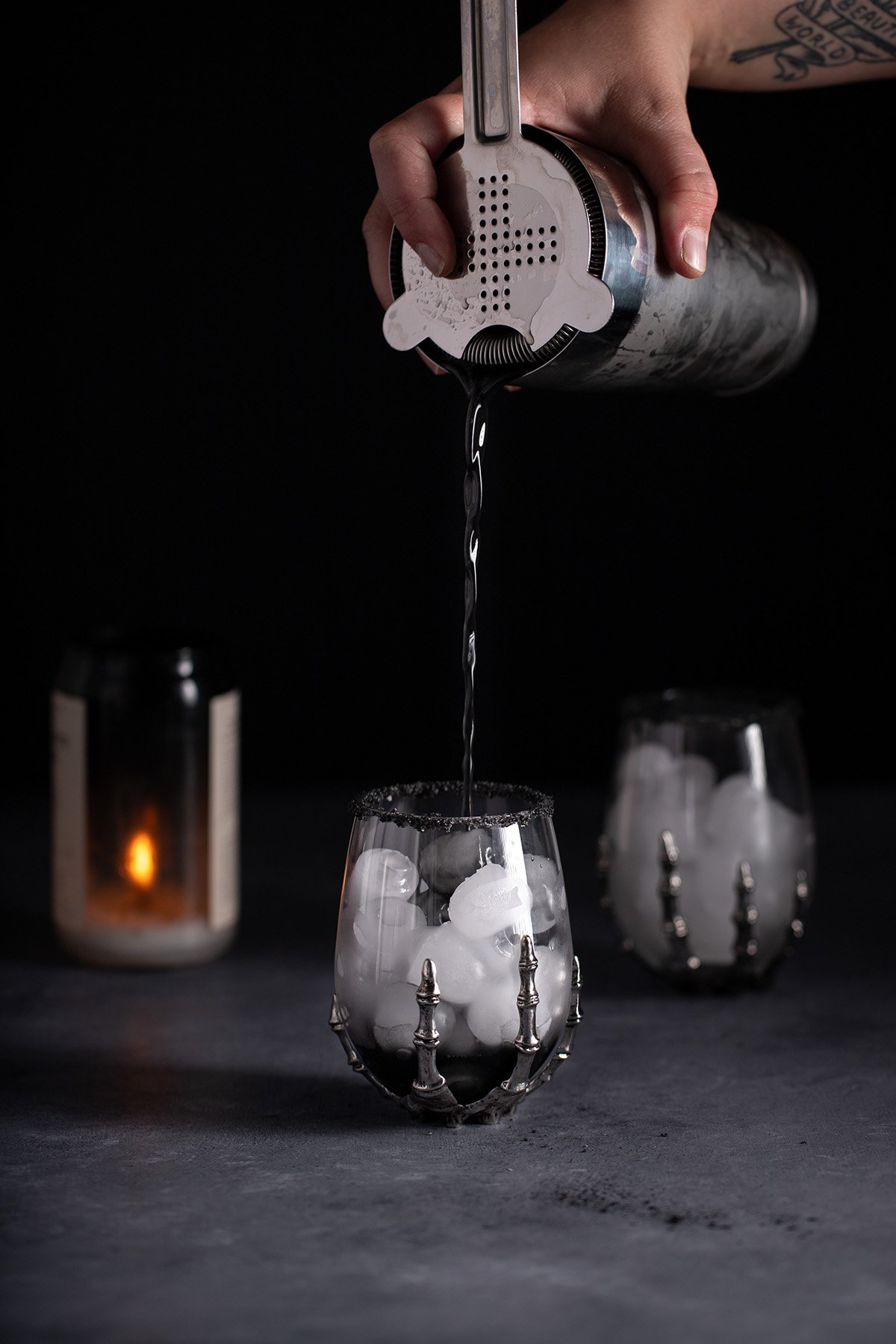 a black margarita being poured into a halloween wine glass.