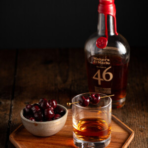 a short glass of bourbon garnished with two bourbon cherries.