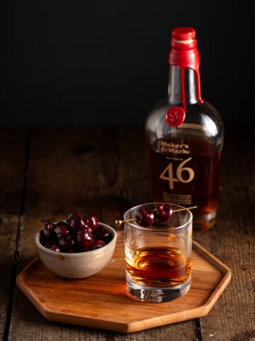 a short glass of bourbon garnished with two bourbon cherries.