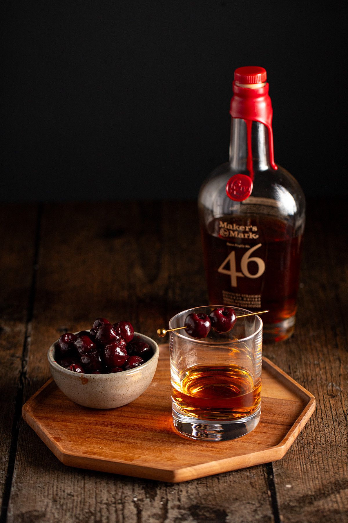 a short glass of bourbon garnished with two bourbon cherries.