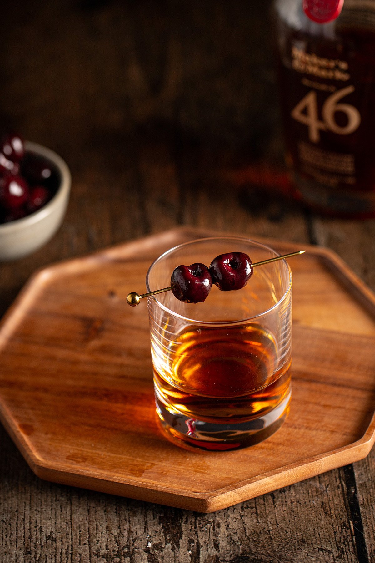 a short glass of bourbon garnished with two bourbon cherries.