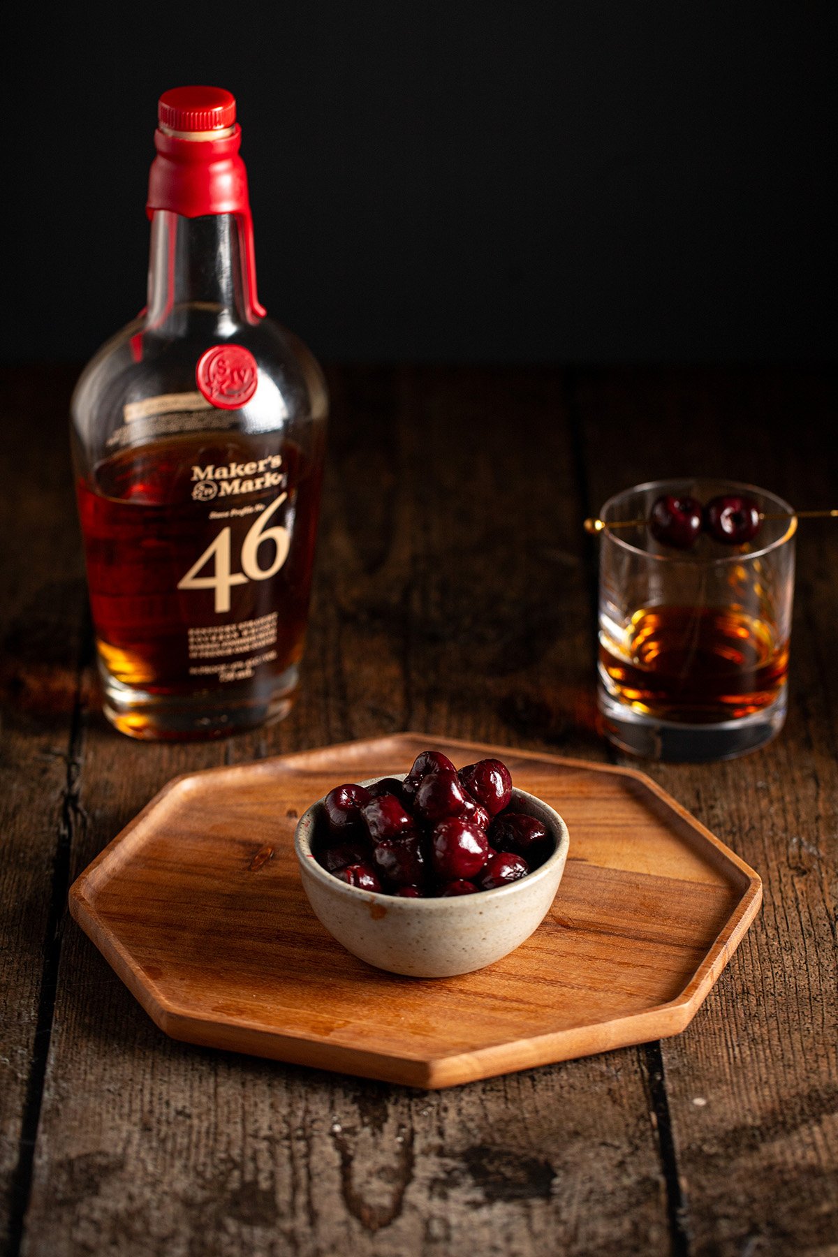 a small bowl of bourbon cherries on a wooden tray.