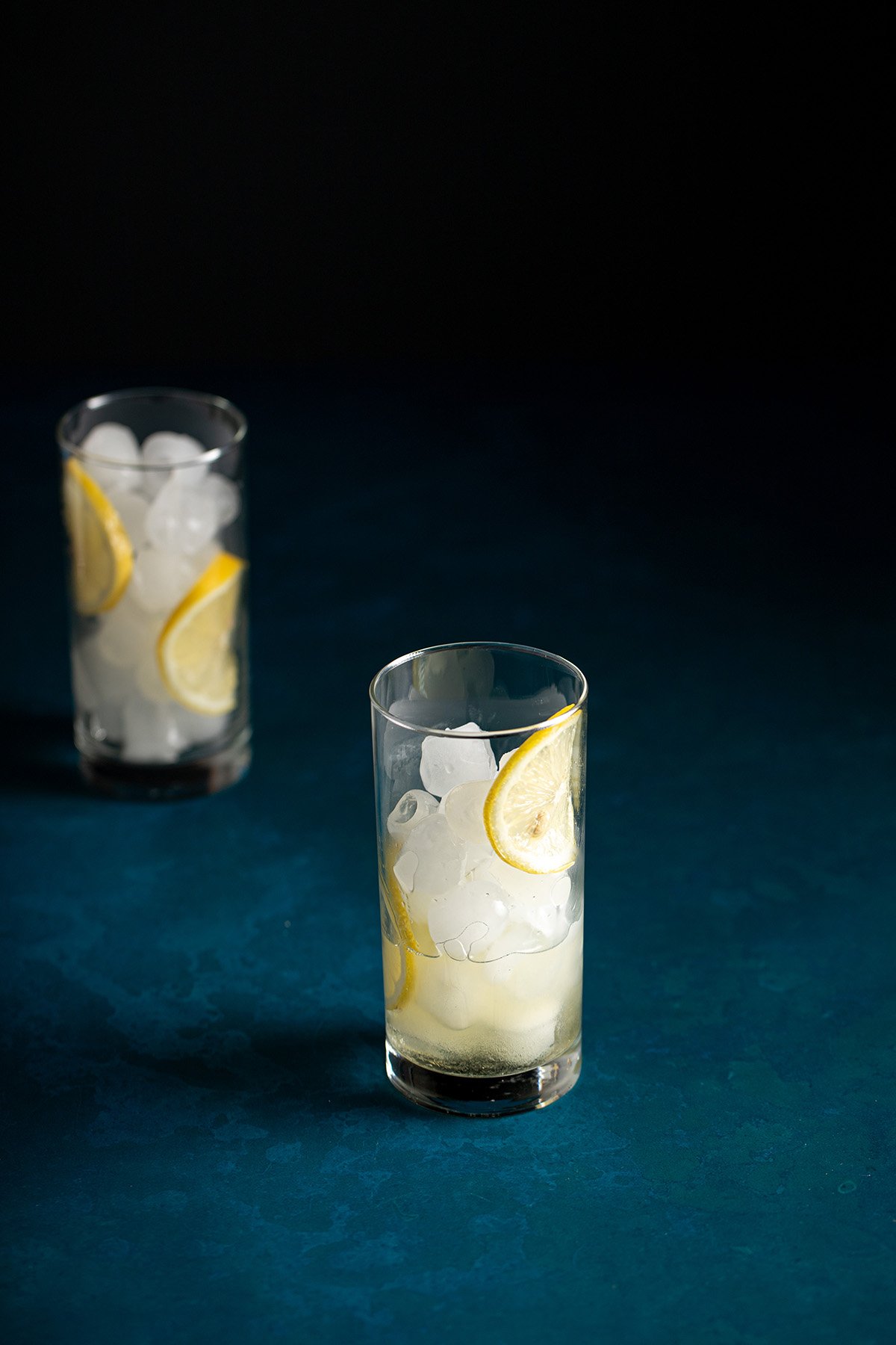 a tall glass filled with ice and lemon wheels, lemon juice and simple syrup in the bottom of the glass.