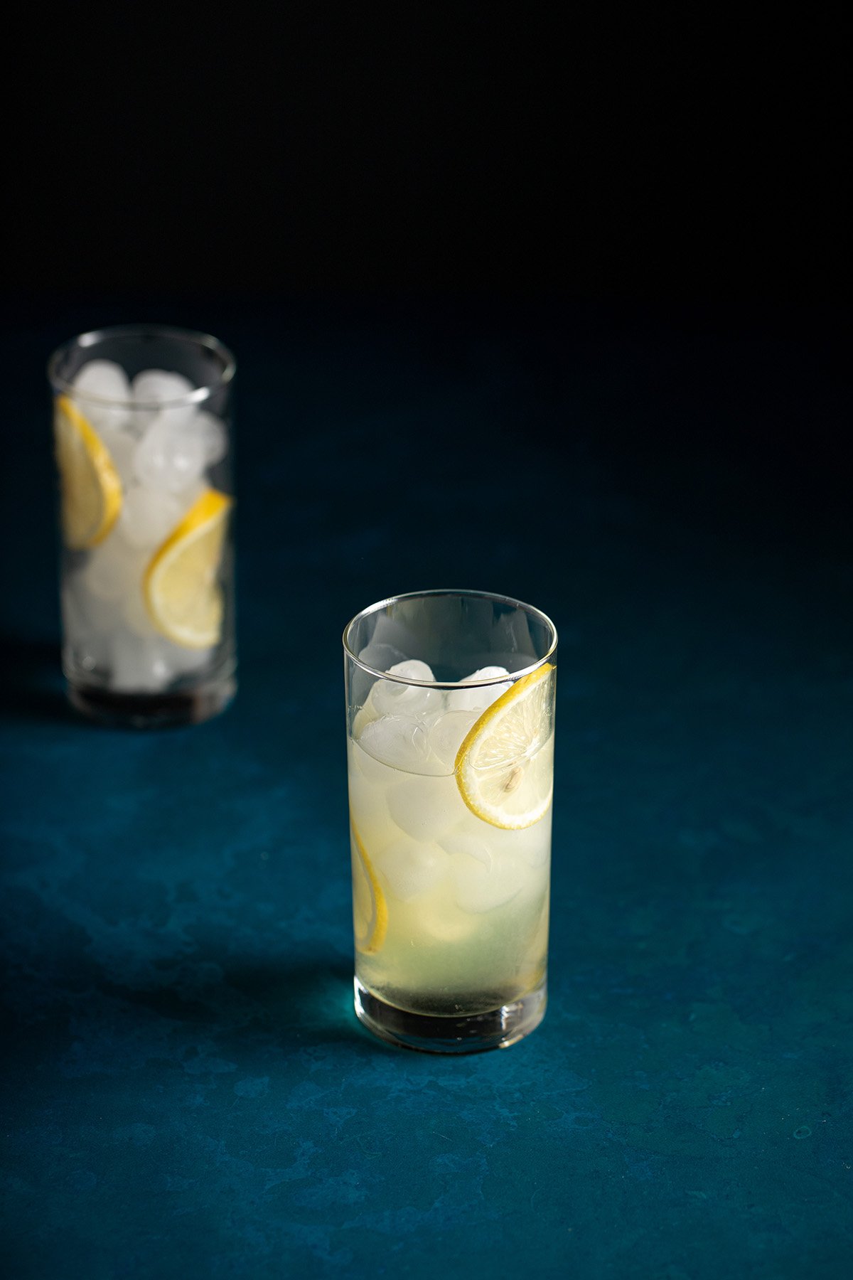 a tall glass filled with ice, lemon wheels, lemon juice, simple syrup, and limoncello and gin.