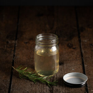 a small jar full of rosemary simple syrup, the lid has been removed.