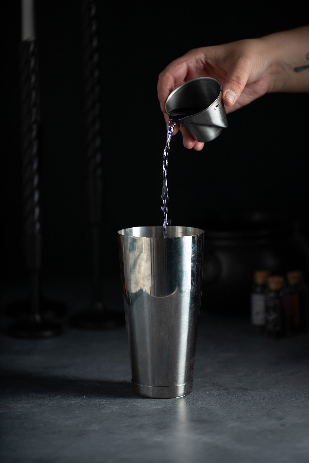 purple gin being poured into a cocktail shaker.