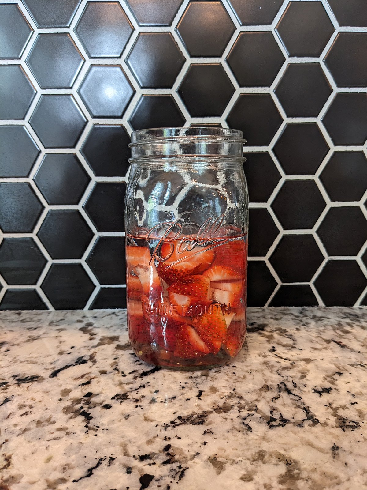 a mason jar full of sliced strawberries and vodka.