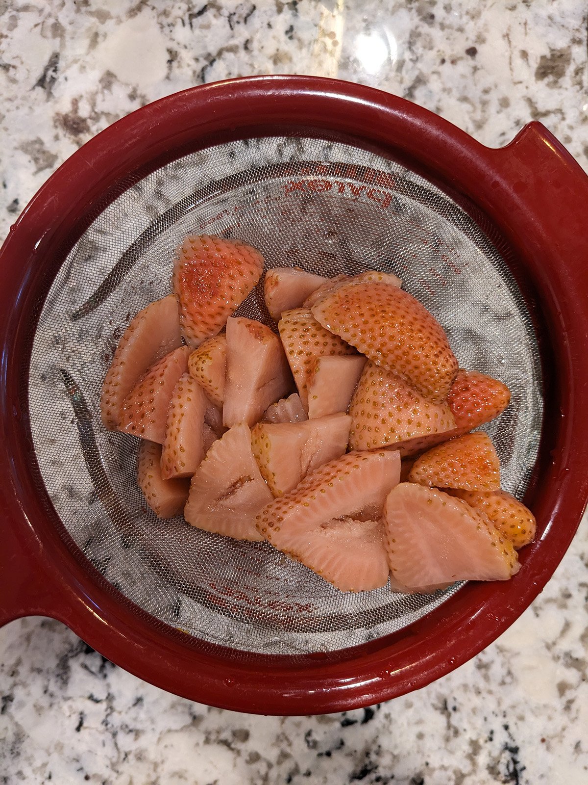 strawberries in a mesh strainer; the strawberries are pale in color.