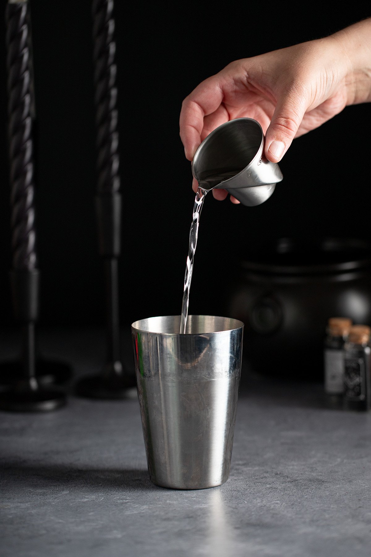 pouring orange liqueur into a cocktail shaker.