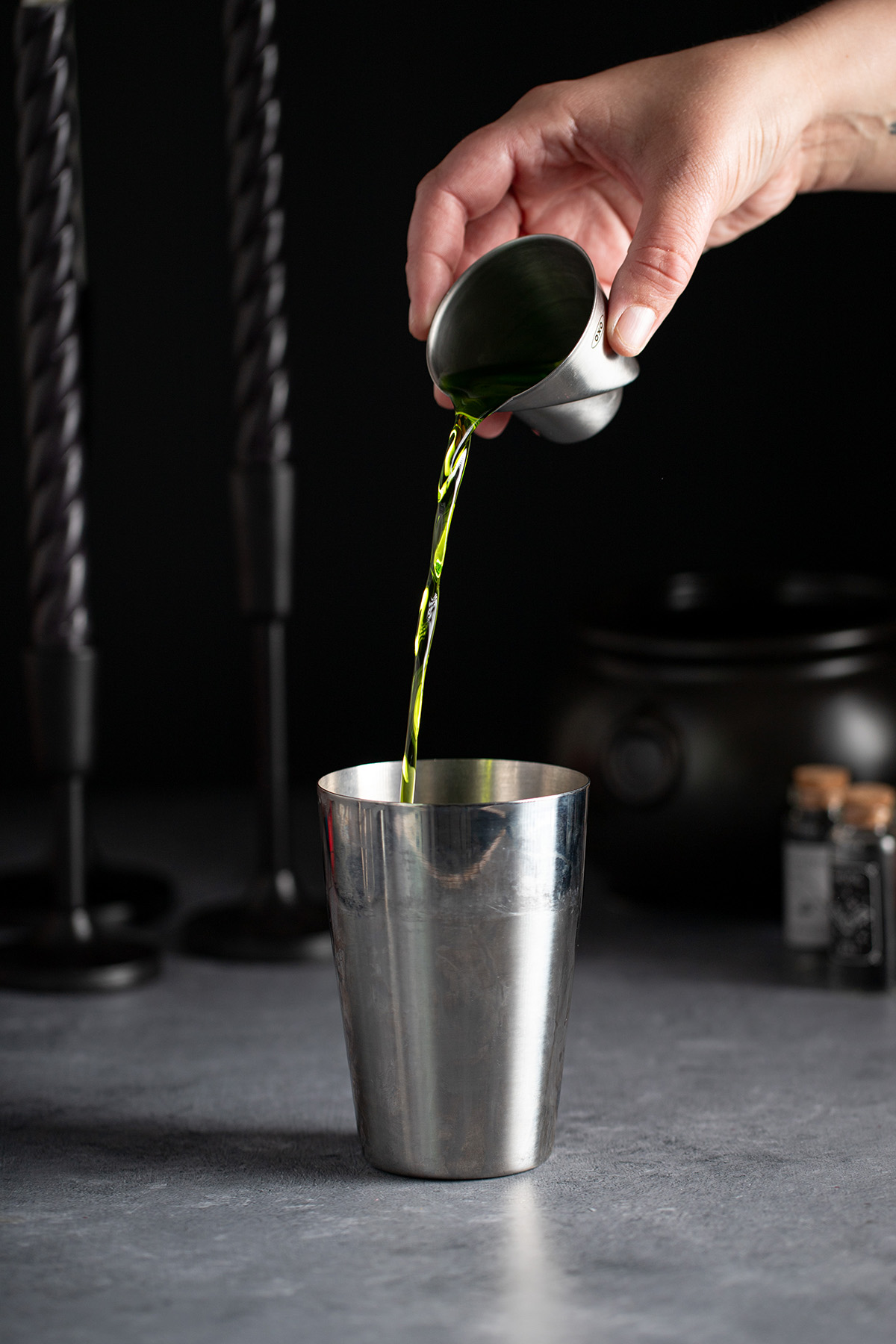 pouring midori liqueur into a cocktail shaker.