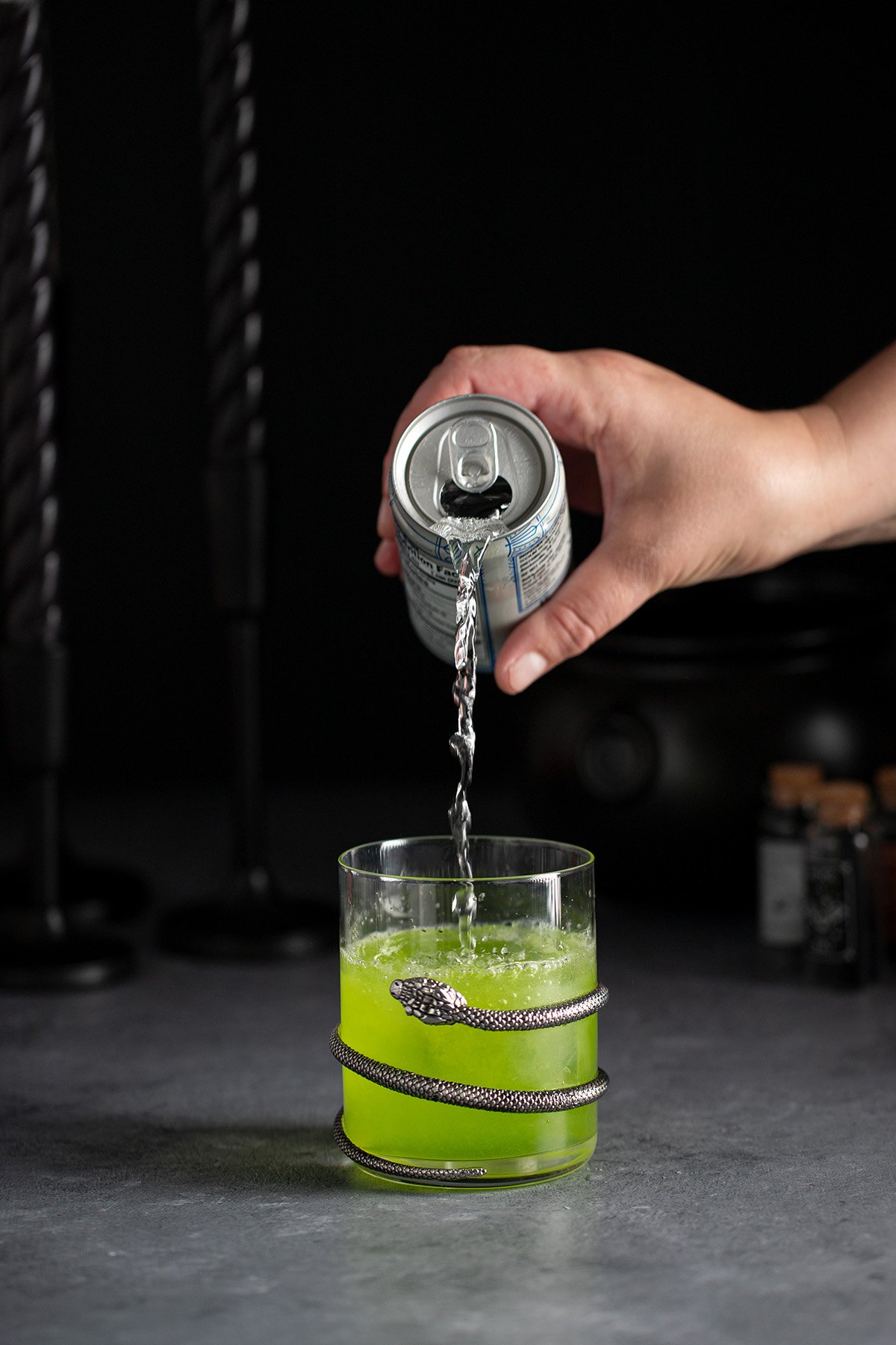 pouring club soda into a witches brew cocktail in a short glass.