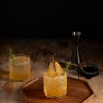 2 ginger pear holiday mocktails in short glasses, garnished with a slice of pear and sprig of rosemary.
