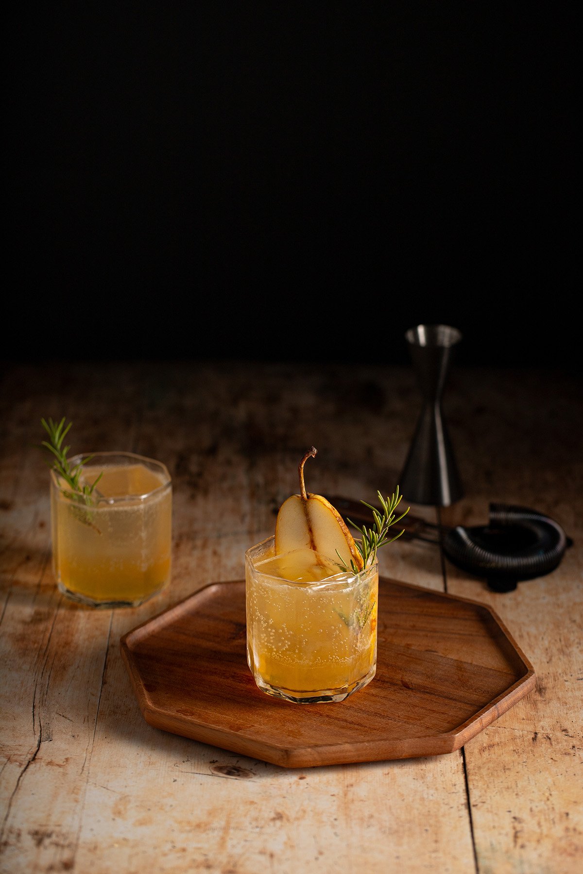 2 ginger pear holiday mocktails in short glasses, garnished with a slice of pear and sprig of rosemary.