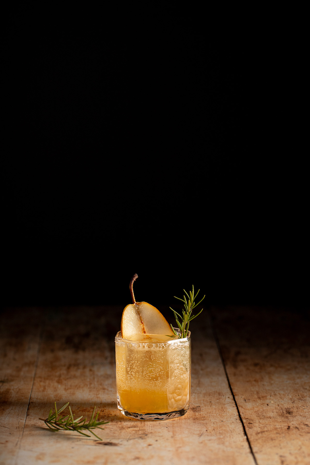 a ginger pear holiday mocktail in a short glass, garnished with a slice of pear and sprig of rosemary.
