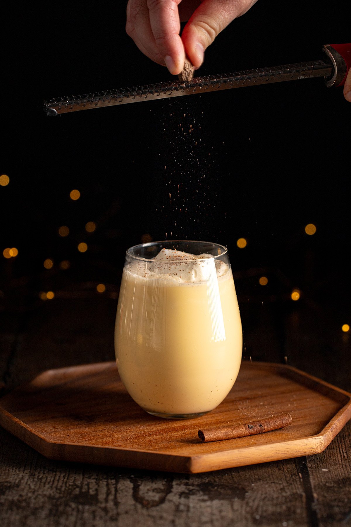 grating nutmeg onto a glass of eggnog with whipped cream.