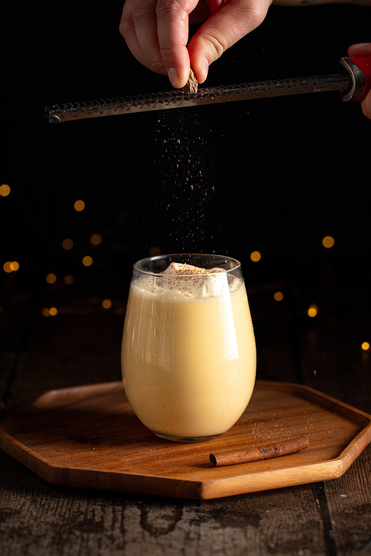 grating nutmeg onto a glass of eggnog with whipped cream.