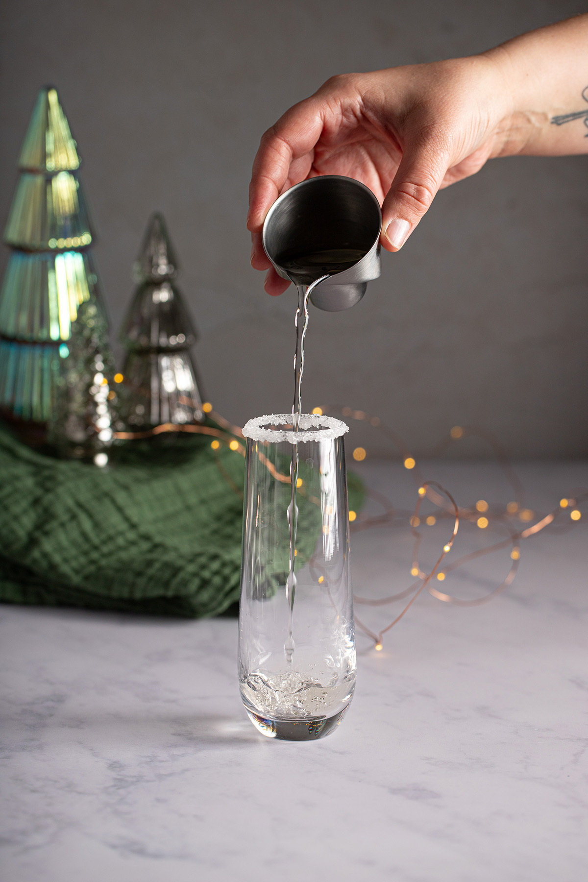 white cranberry juice being poured into a stemless champagne flute rimmed with sugar.