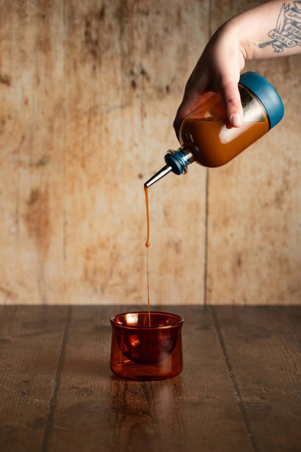 a hand pouring a small bottle of carrot cake syrup into a small amber glass.