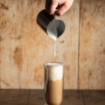 cold foam being poured onto a glass full of an iced latte.