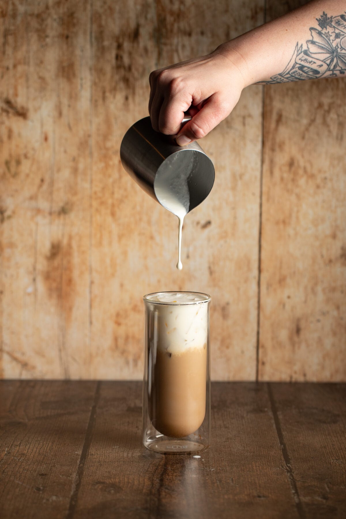 cold foam being poured onto a glass full of an iced latte.