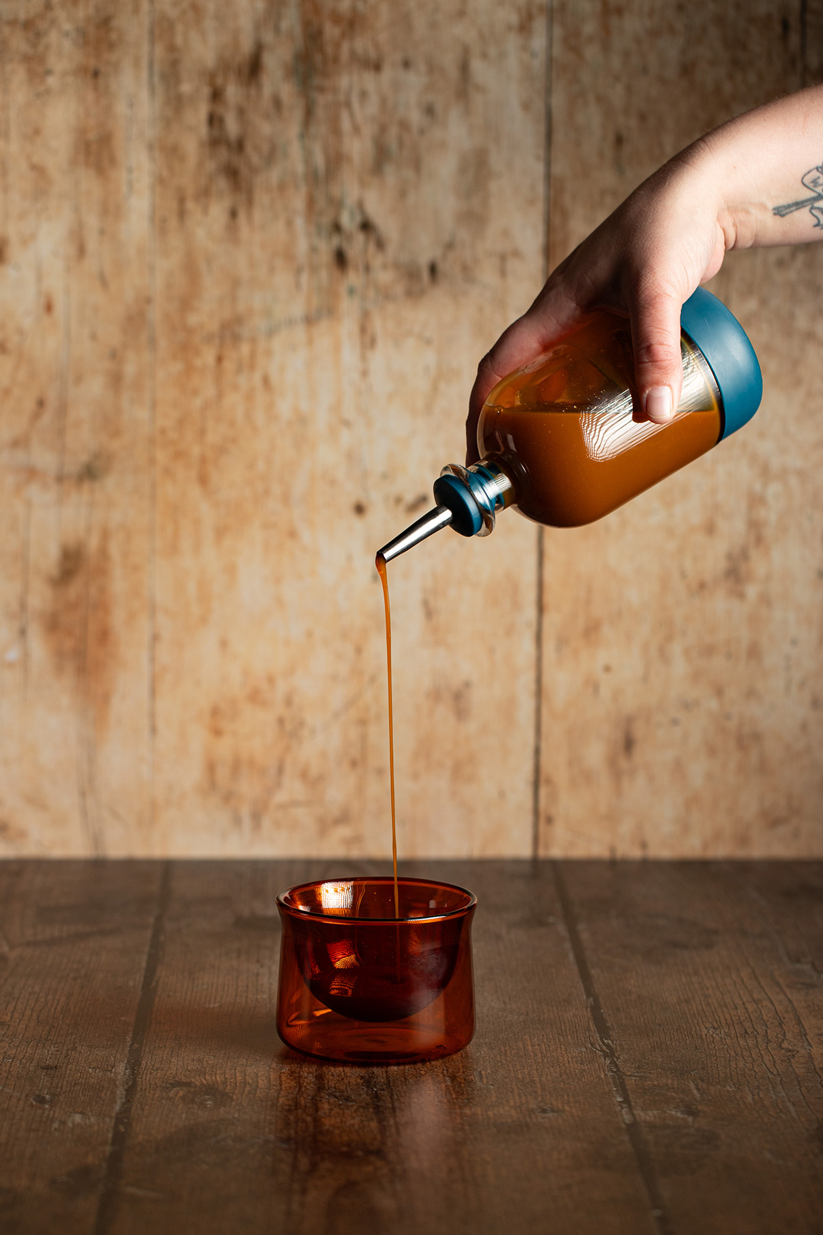a hand holding a small bottle, pouring carrot cake syrup into a small amber colored glass.